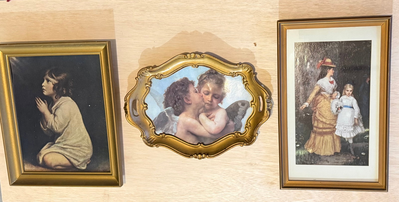 Three Framed Vintage Oil Print Wall Decorations: Collection of three vintage framed oil print wall decorations featuring sentimental figural scenes in the European taste. The group includes a praying child portrait, a cherub scene within an ornate