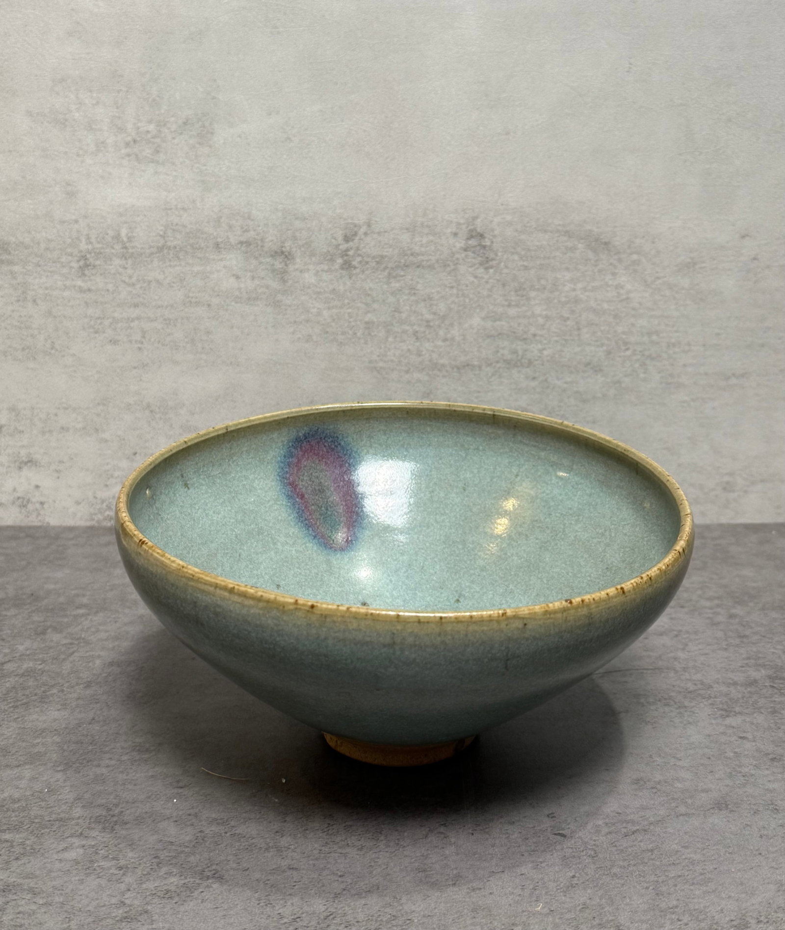 Chinese Celadon Glazed Pottery Bowl: Chinese pottery bowl featuring a soft celadon glaze accented by a lavender-purple splash to the interior. The bowl is potted in a graceful rounded form with subtle foot ring and displays an attractive
