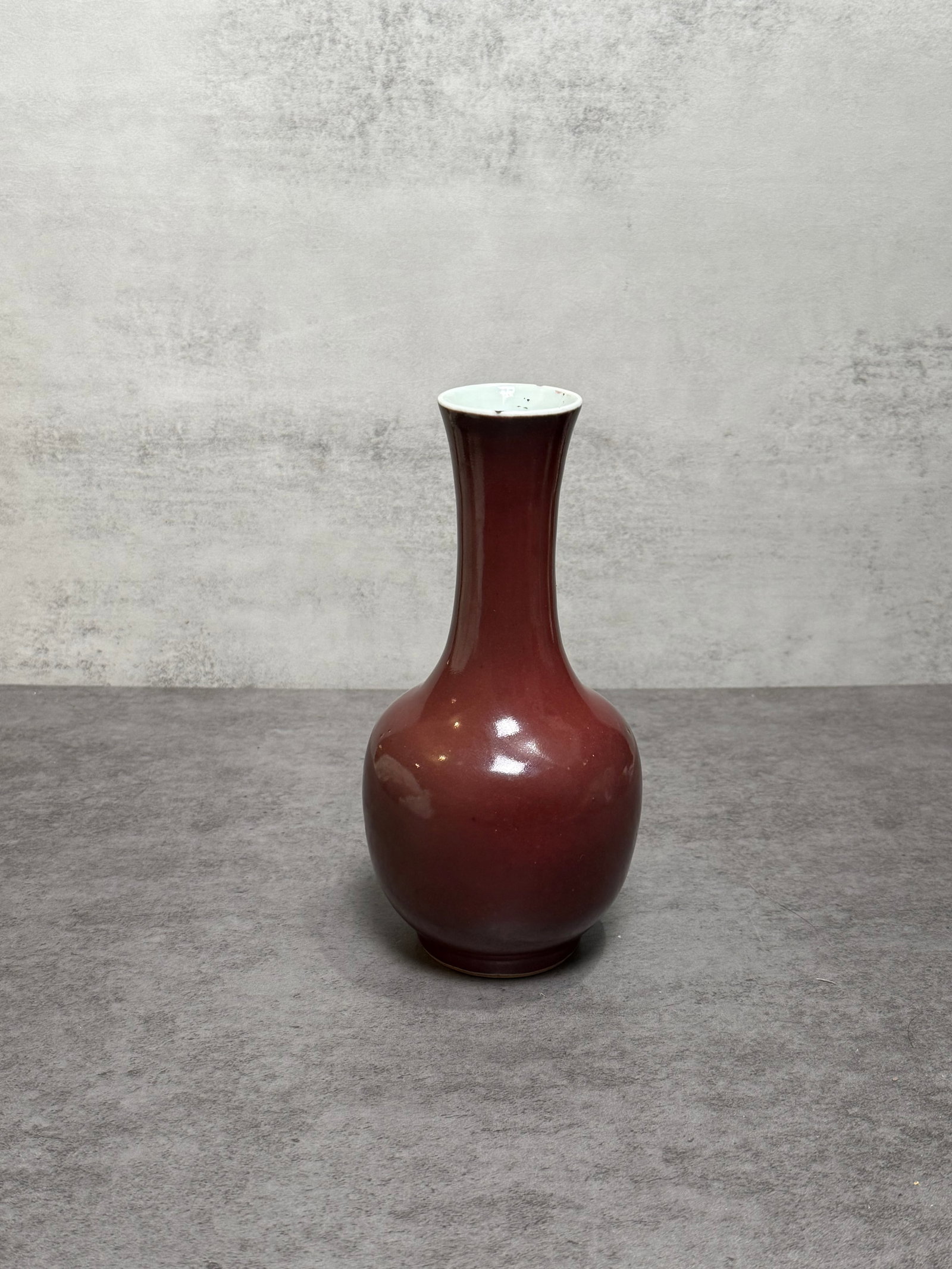 Chinese Oxblood Glazed Porcelain Bottle Vase: Chinese porcelain bottle vase featuring a rich oxblood-style glaze in deep sang-de-boeuf tones. The vase is potted with a rounded body rising to a slender elongated neck, covered in a lustrous