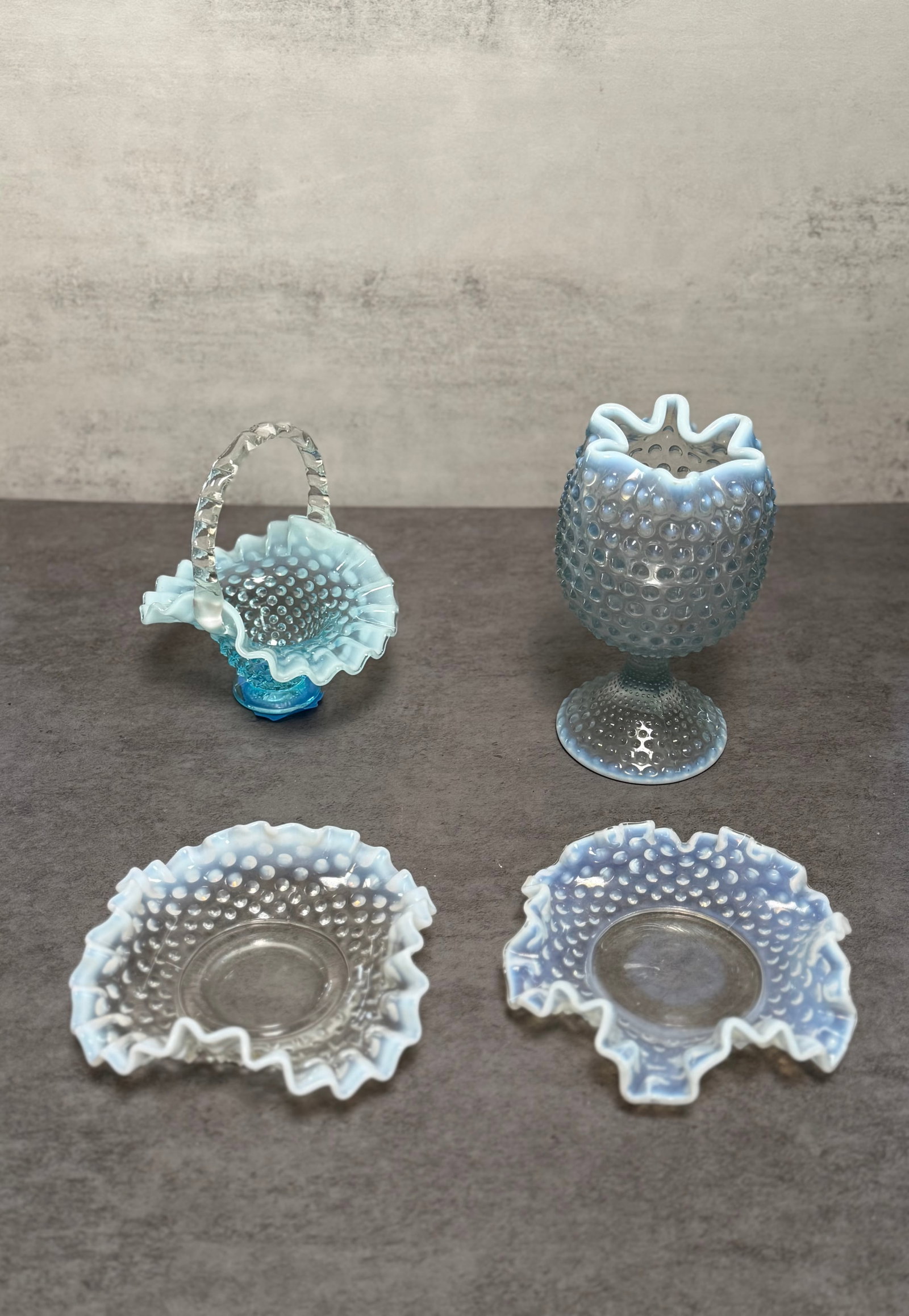 GROUP OF OPALESCENT HOBNAIL GLASS TABLE ARTICLES: A group of four opalescent hobnail glass table articles, including a miniature basket with clear applied handle, a footed vase or toothpick holder, and two ruffled dishes with crimped edges. The piece