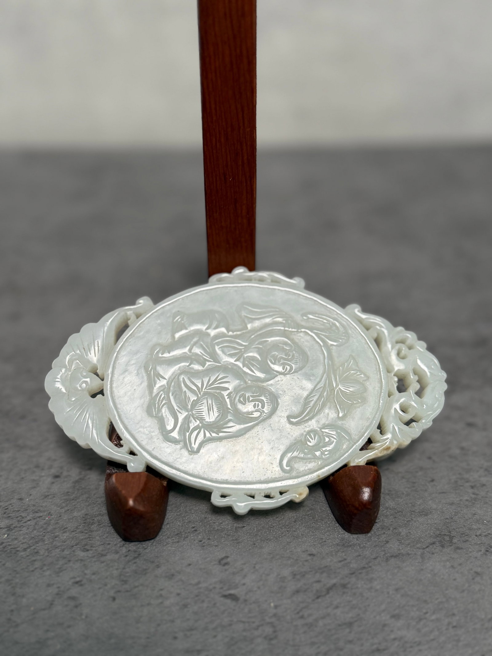 CHINESE OPENWORK JADE CARVED PLAQUE WITH FIGURAL MOTIF: A Chinese carved pale celadon jade plaque of oval form, featuring finely incised figural decoration to the center, framed by openwork scrolling borders with floral and foliate motifs. The stone