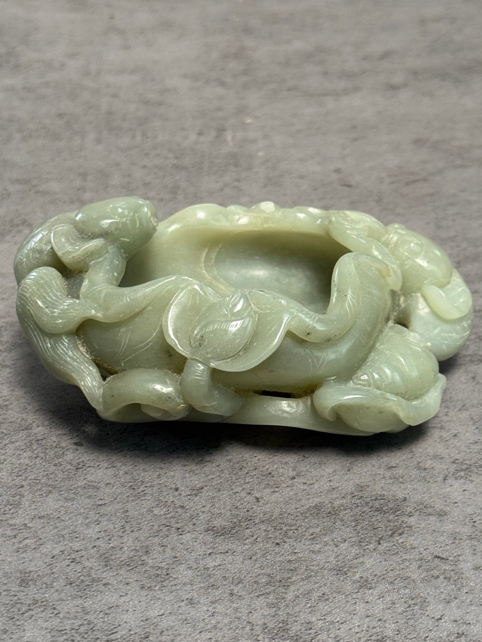 CHINESE JADE CARVED BRUSH WASHER WITH LOTUS MOTIF: A Chinese pale celadon jade carved brush washer of oval form, surrounded by openwork lotus vines, leaves, and pods in high relief. The stone displays soft translucent green coloration with natural