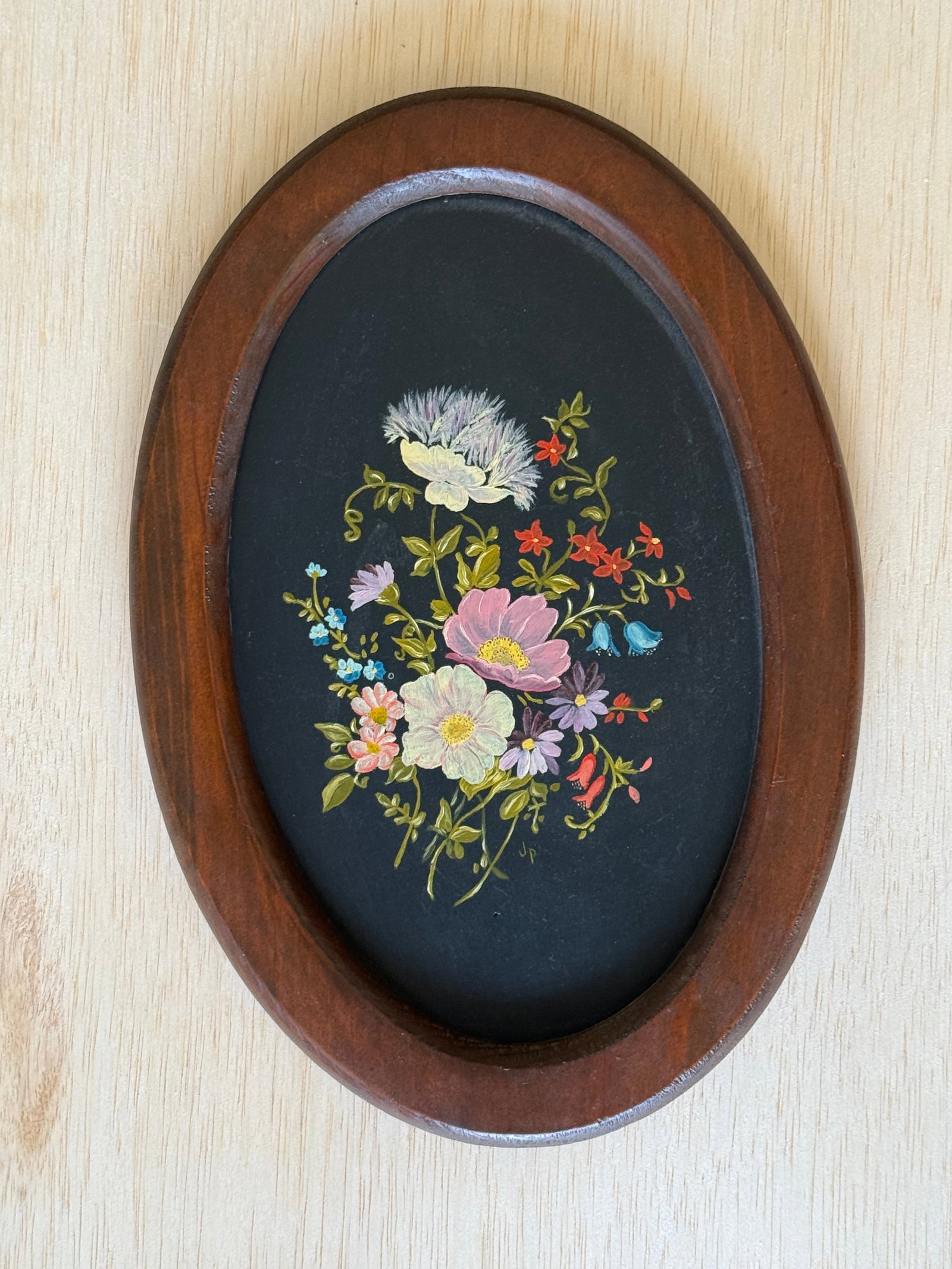 Hand-Painted Floral Still Life Plaque In Oval Wooden Frame: Delicate hand-painted floral composition featuring assorted blooming flowers against a black ground, housed in an oval wooden frame. Executed in a folk art and Victorian-inspired manner with colorful