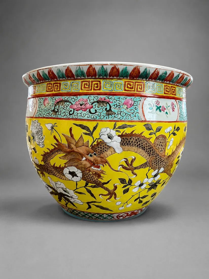 Chinese Famille Rose Yellow Ground Dragon Fish Bowl / Jardiniere: A large Chinese famille rose porcelain fish bowl or jardiniere featuring a vibrant yellow ground decorated with a five-clawed dragon in pursuit among flowering branches. The rim is accented with tradi