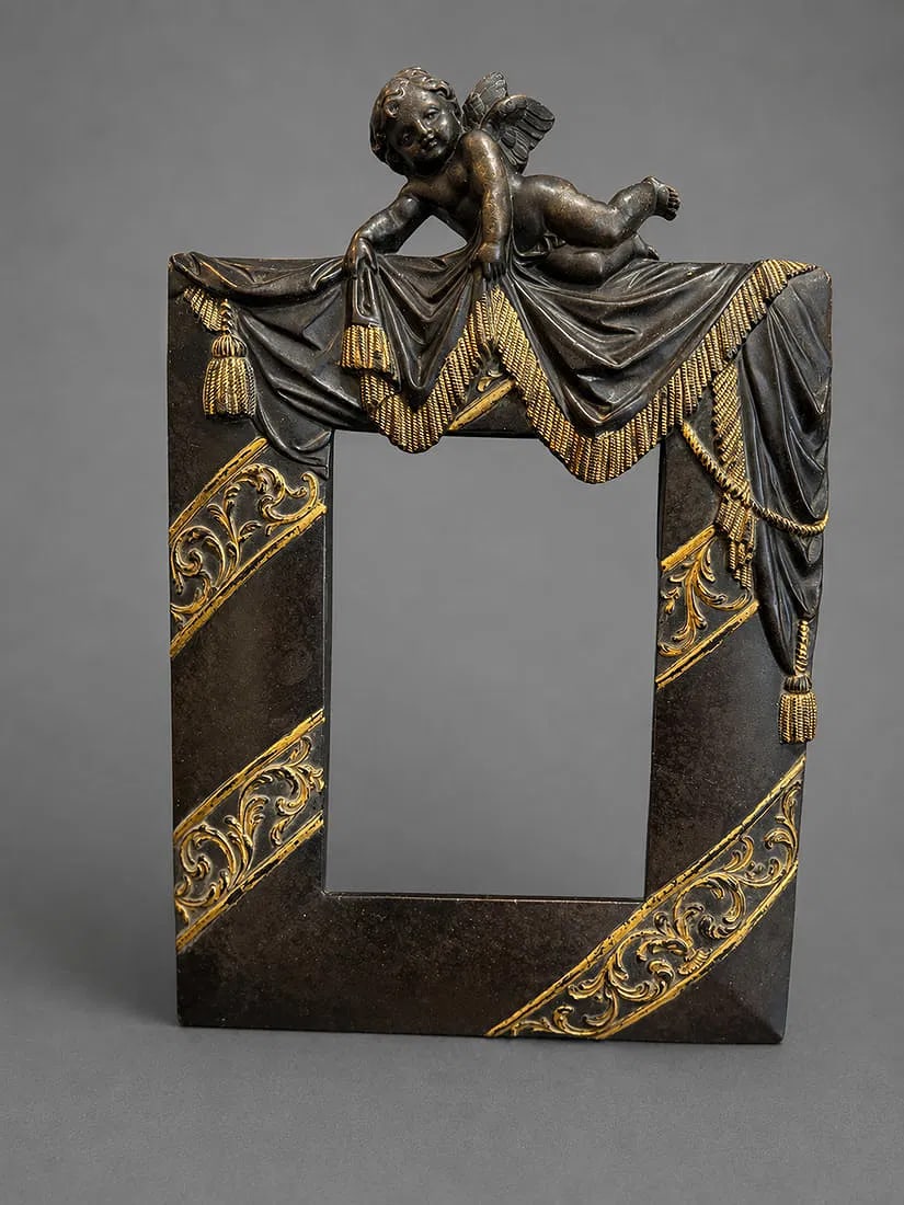 Carved Wood Picture Frame with Cherub Motif: A decorative carved wood picture frame featuring a reclining winged cherub resting atop an elaborately draped fabric adorned with tassels. The frame is embellished with raised gilt scrolling decoratio