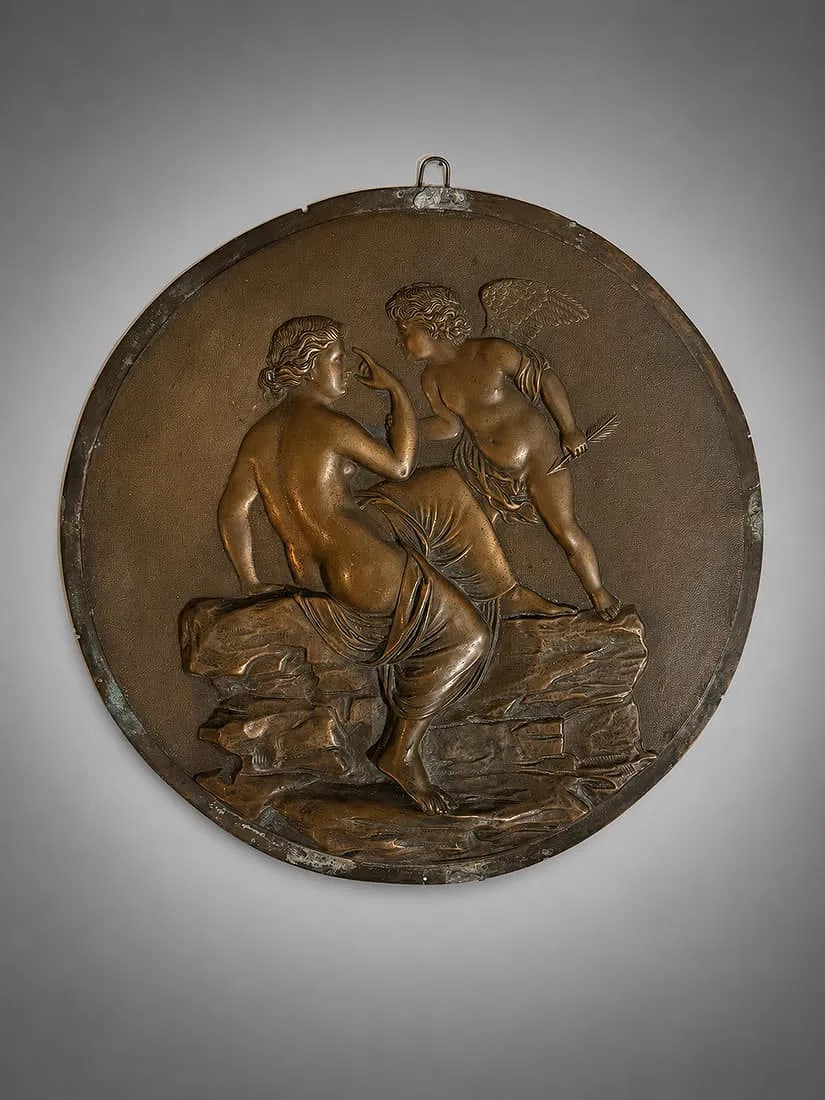 Classical Figural Bronze Relief Wall Plaque Depicting Venus and Cupid: Round relief wall plaque depicting a classical mythological scene of Venus and Cupid. Cast with finely detailed figures in high relief and finished with a warm bronze-tone patina. Features an integrat