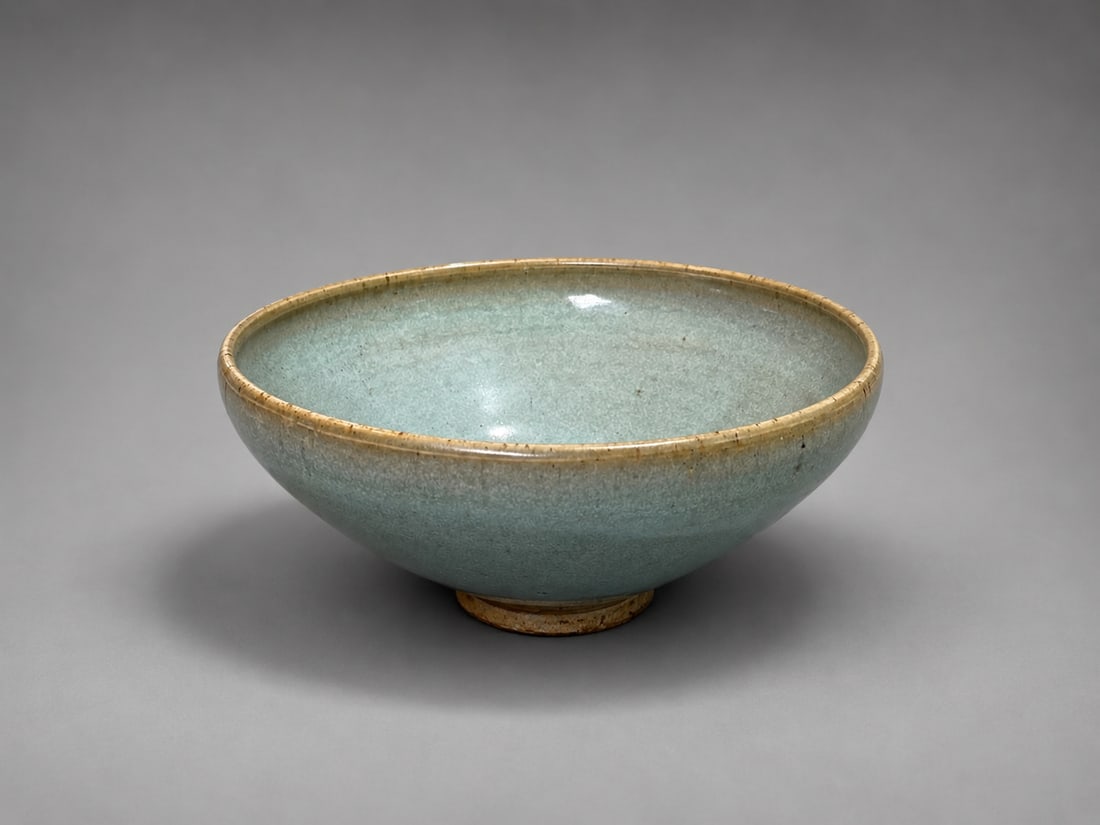 Chinese Jun Ware Glazed Ceramic Bowl: A Chinese Jun ware ceramic bowl of rounded form, supported on a short circular foot. The bowl is covered in a soft blue-green glaze displaying subtle tonal variations, thinning to a warmer tone around