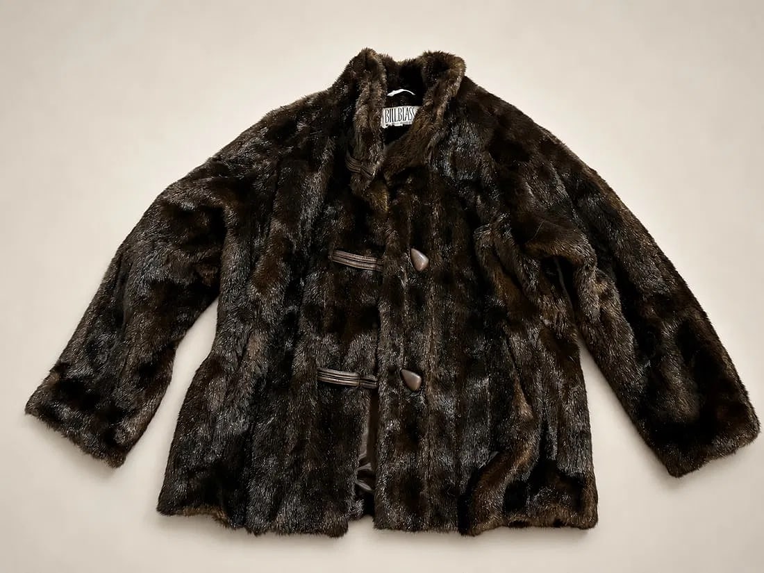 Vintage Bill Blass Faux Fur Coat: Vintage Bill Blass faux fur coat featuring a rich dark brown finish with a soft, plush texture. Designed with a stand collar, decorative toggle-style front closures, long sleeves, and a straight-cut s
