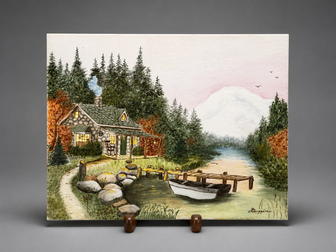 Signed Hand-Painted and Fired Ceramic Landscape Plaque: A decorative ceramic plaque featuring a hand-painted landscape scene depicting a lakeside cottage, boat, wooded surroundings, and distant mountains. The painted decoration appears to have been fired o
