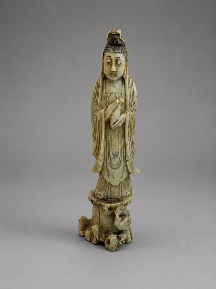 A Chinese Qing Dynasty Shoushan Soapstone Carved Guanyin Figure: A Chinese Qing Dynasty carved Shoushan soapstone figure depicting Guanyin standing in flowing robes, with a serene expression and hair arranged in a high chignon. Finely carved throughout and raised o
