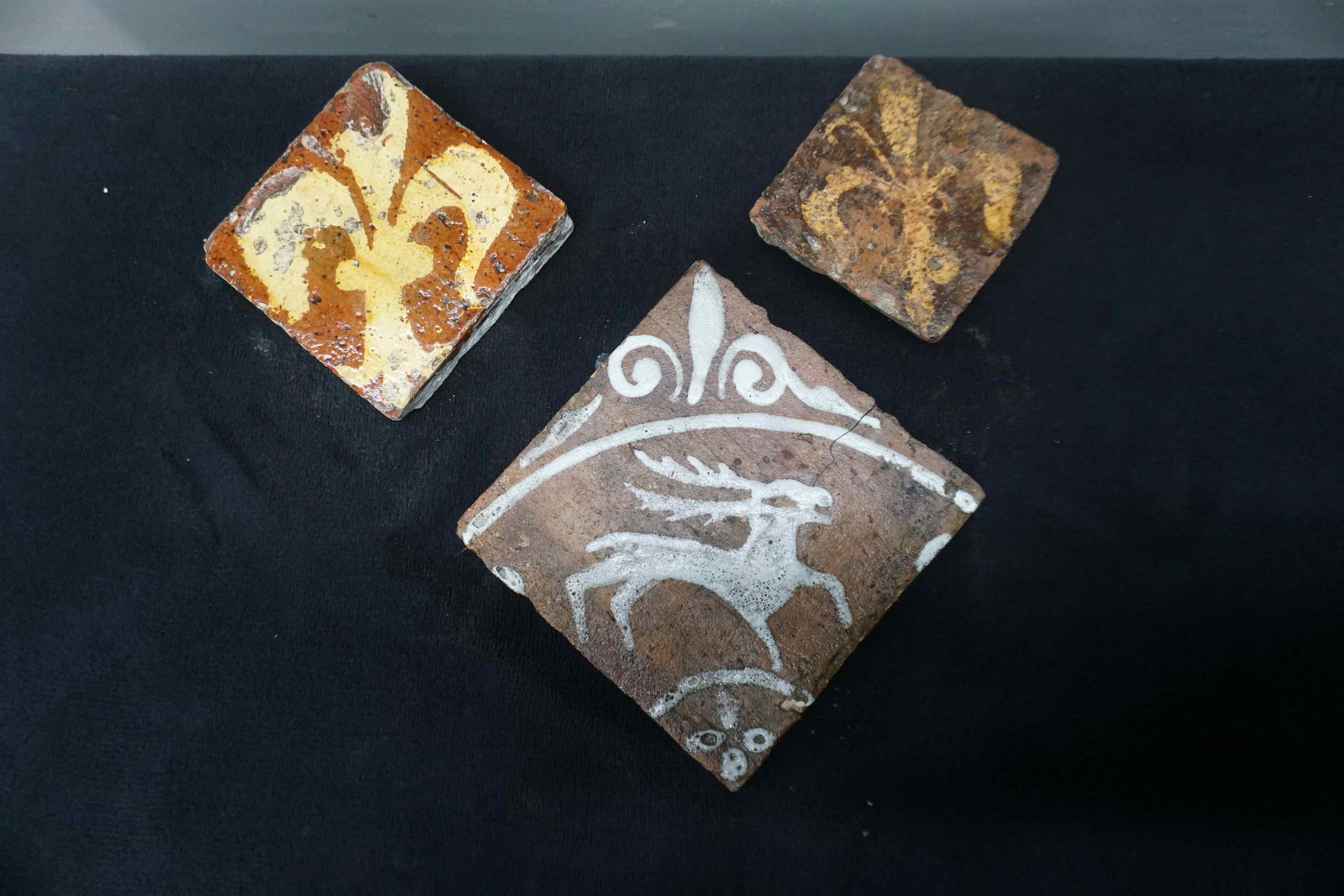 Lot (2) of medieval tiles in glazed slipware with a stylized motif of a French lily, included:: Lot (2) of medieval tiles in glazed slipware with a stylized motif of a French lily, included: decorative tile with deer motif, France 15th H16x16x12x12x10x10
