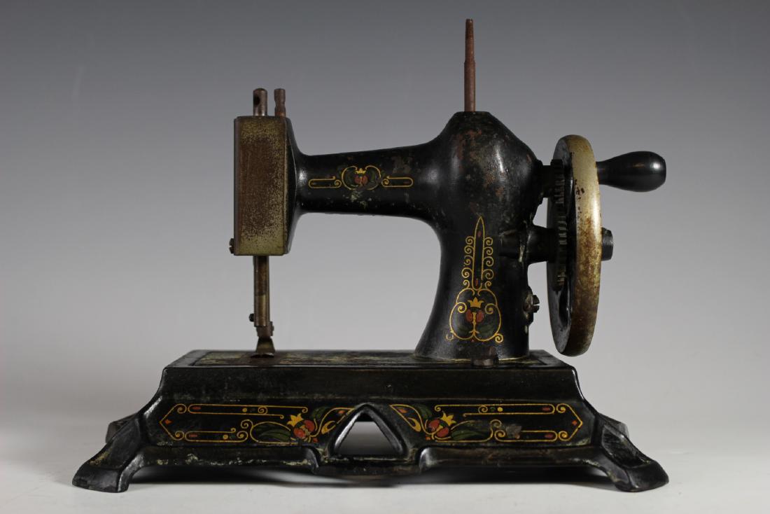 German Antique Childs Sewing Machine: Cast iron antique child's sewing machine marked Made In Germany. Approx. 8"t by 9.5"w. Having original black finish and stenciling. In good working condition, having paint loss throughout and some sur