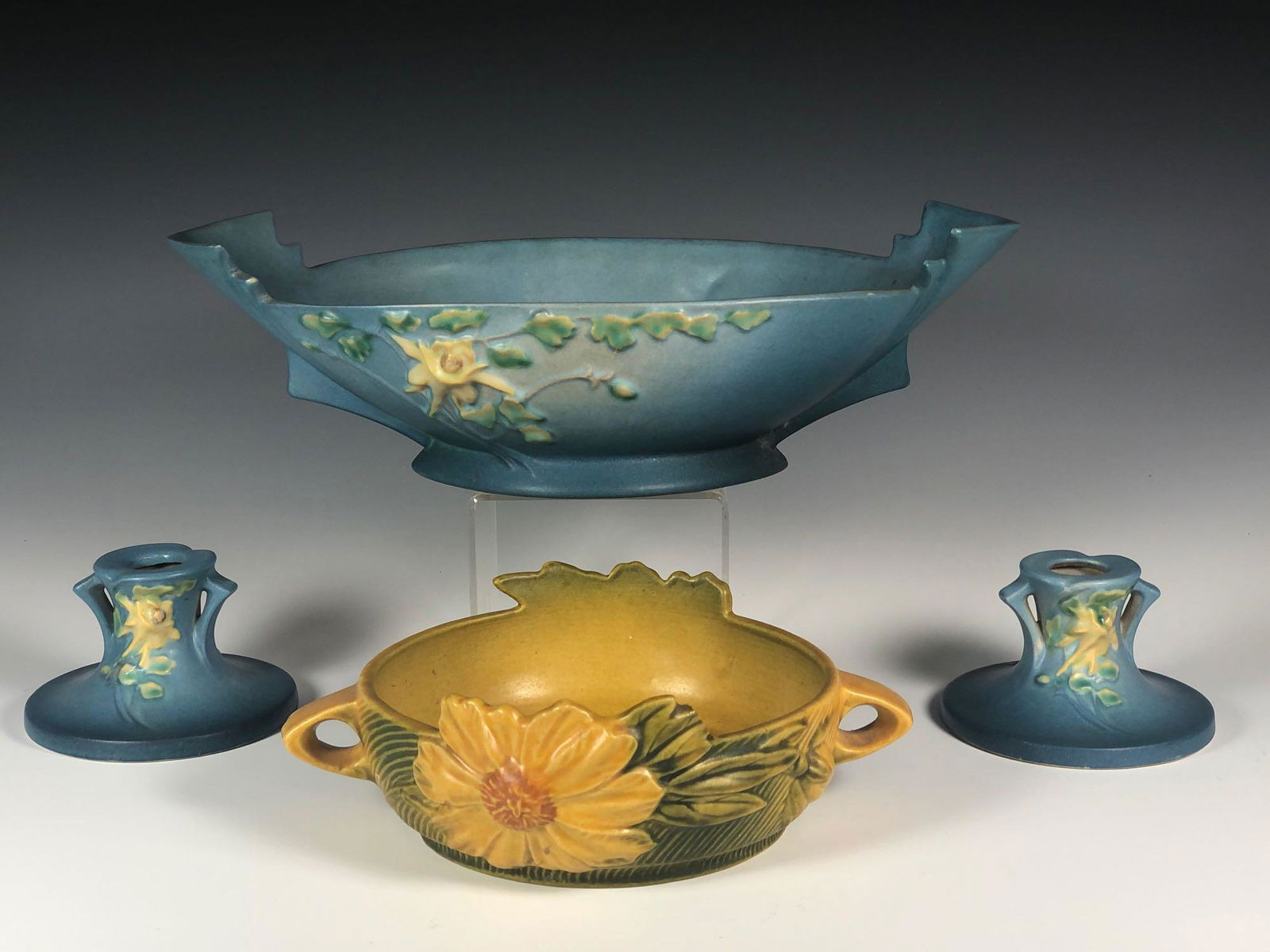 Collection of Four Roseville Pieces: Collection of five Roseville pottery including; pair of candlesticks 1145 approx. 2.5", sunflower double handled bowl 428 approx 6" with chip off flower leaf see photos and blue large dish 405 approx