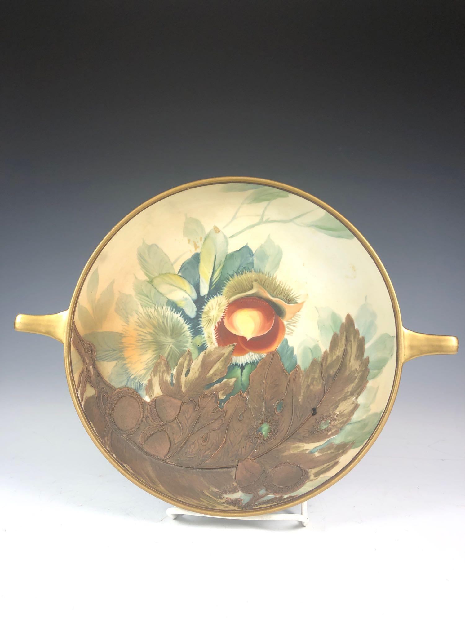 Nippon Double Handle Bowl With Raised Relief: Fine Nippon low nut or candy bowl with raised relief, acorns, gold gilt edge and handle's with foliage design. Condition very good. H. 2'' Diam 8 1/2'' to handle's 11''.