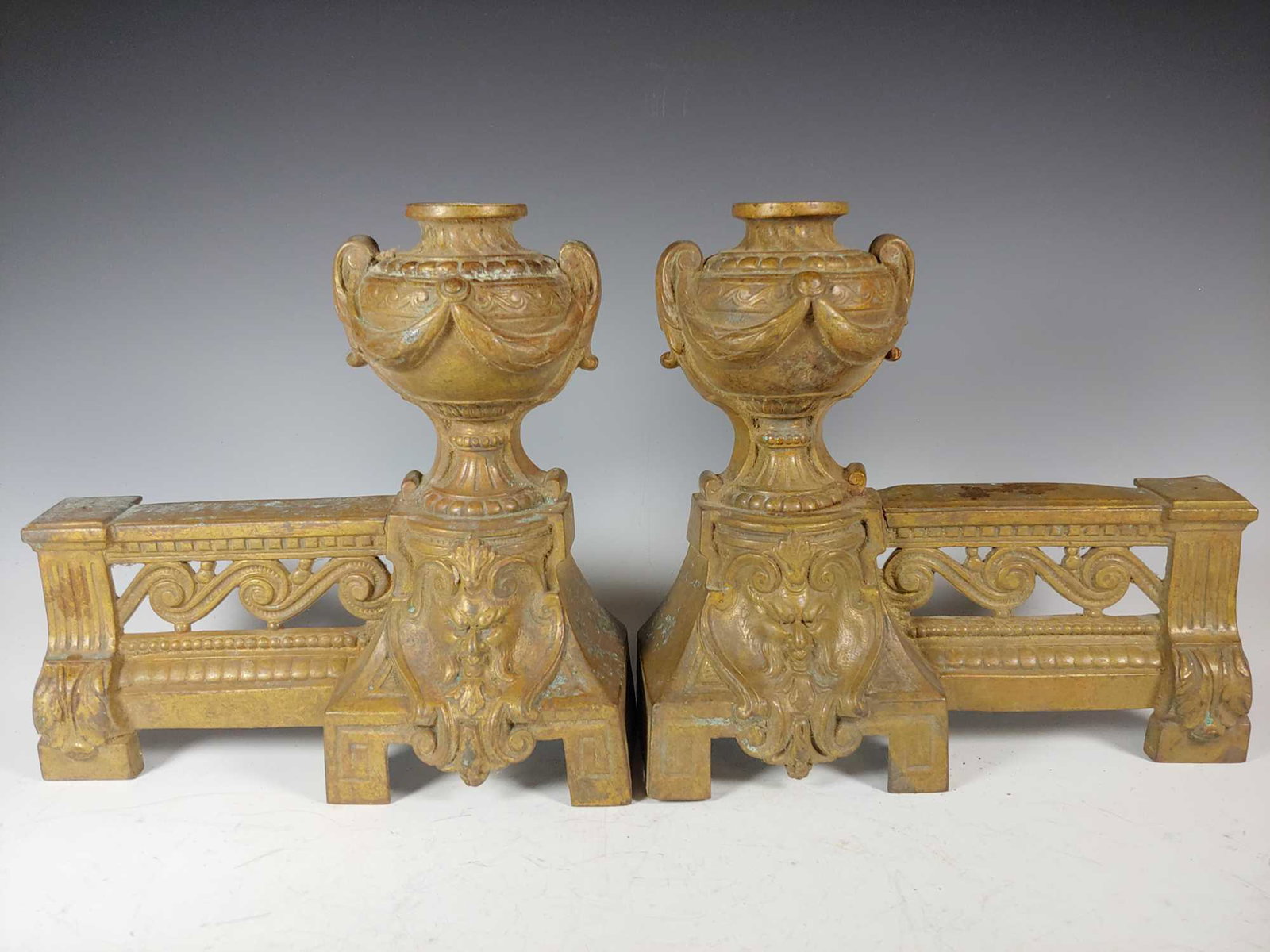 Pair of Antique Brass Urn Demon Face Andirons: Late 19th early 20th century andirons depict demon faces at base below urns. Approx. 9" tall by 9 1/4" deep. In good age appropriate condition with signs of age, see photos.