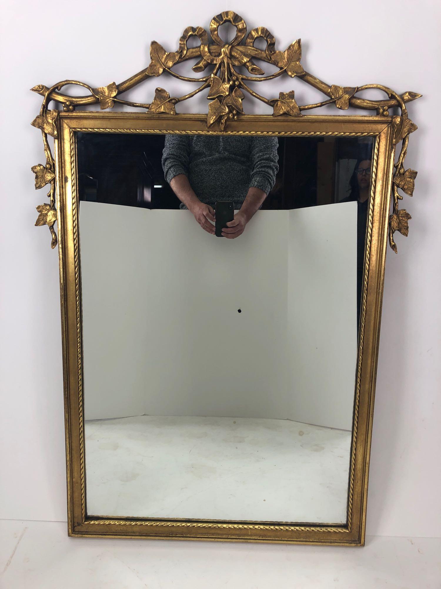 20 th C. Hollywood Regency MCM gold Tone Leaf Bow: 20 th C. Hollywood Regency MCM Gold Tone Leaf Bow Design Wooden Wall Hanging Mirror. Good overall condition with no chips or cracks. Minor impeferfection / nick on left hand side if facing mirror. Ple