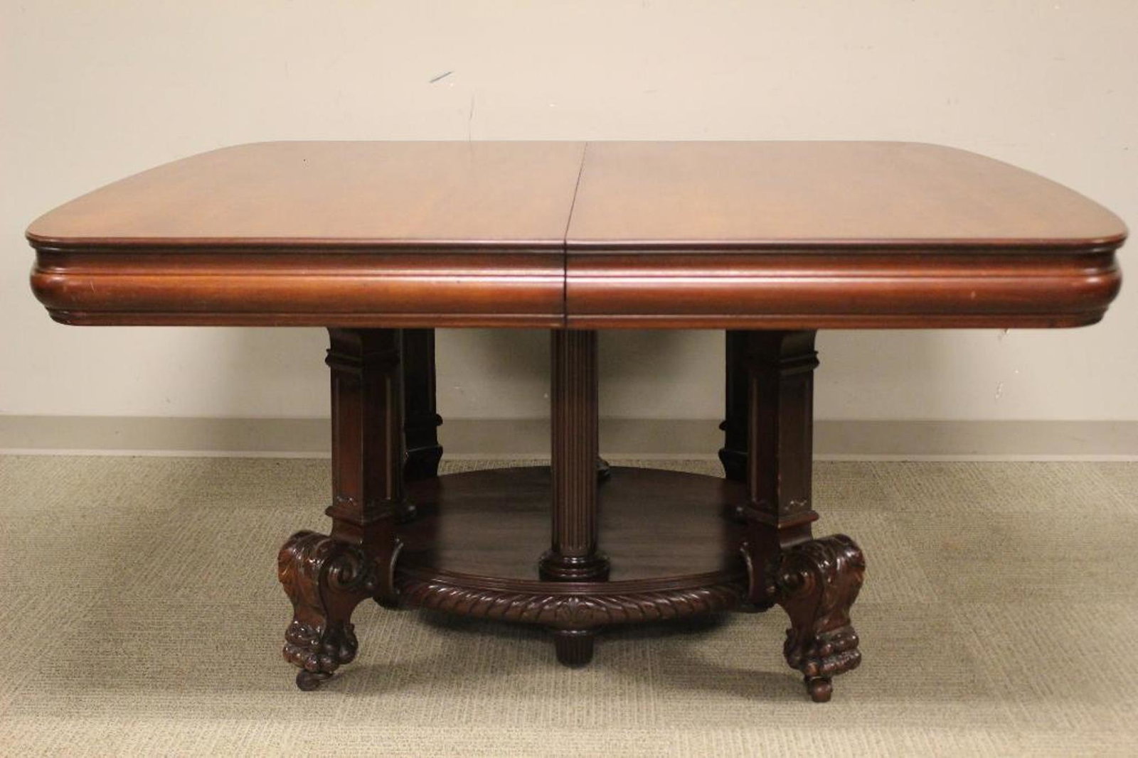 Massive 12ft Carved Mahogany Empire Dining Table: Featuring a massive 54" wide having seven (7) skirted leaves allowing the table to open to 12ft in length. The carved claw foot roman greco curved foot. Table also fitted with custom magnetic table co