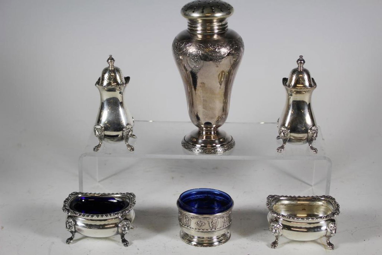 Silver Plate and Sterling Grouping: Group includes; Wilcox silver plate ornate sugar shaker, Ellis Bros lion head and feet salt and pepper shakers, Ellis Bros lion head and feet salt cellars one with chip cobalt glass liner and Wallace 