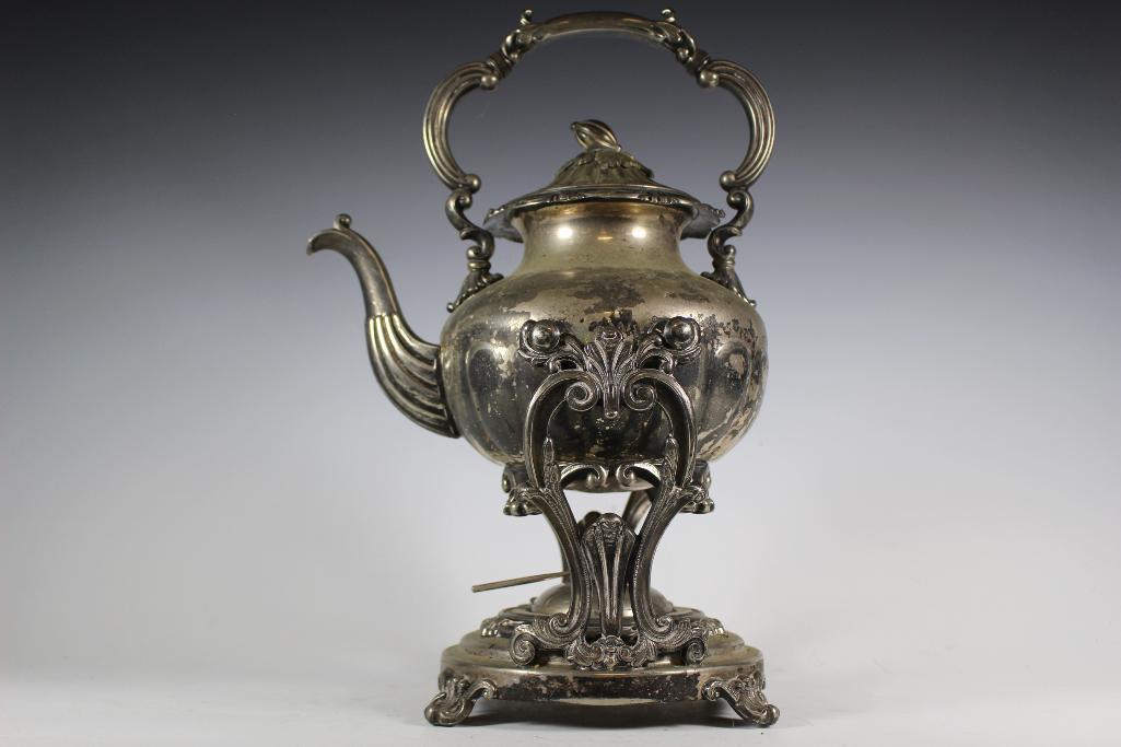 Antique Silver on Copper Teapot on Stand: Ornate silver plate teapot on tilting stand with burner. Having leaf and flower bud lid with four hallmarks on base of teapot. Approx. 15 1/2" tall overall with footed teapot and footed stand. In age
