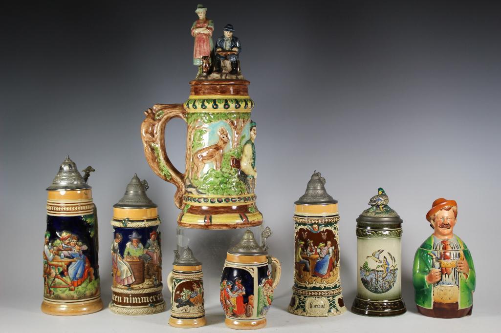 Collection of 8 Beer Steins Tankards: large group of German beer steins ranging from 5" to 15 3/4" tall. All depicting German scenes, figures and animals. Largest is all porcelain with porcelain with chip to lid and tree branch squirrel h