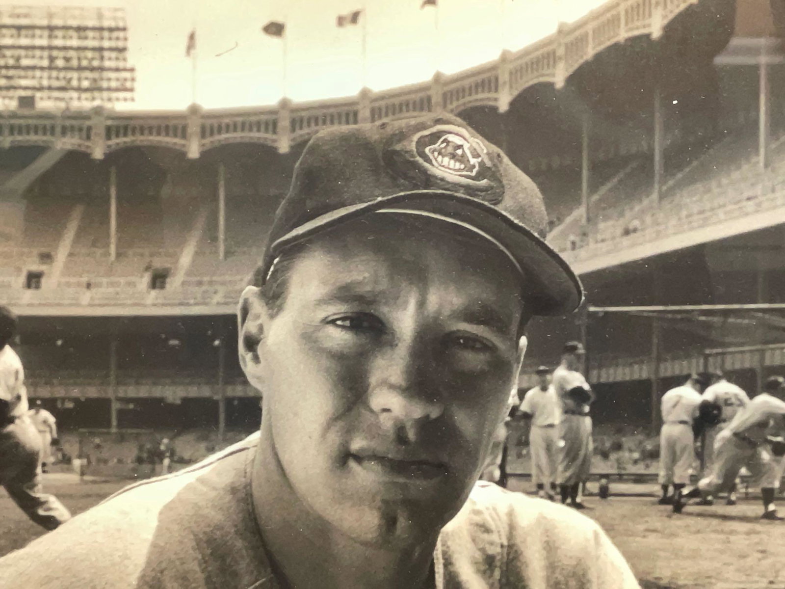 GRACEFUL BLACK AND WHITE FRAMED PHOTO OF BOB FELLER in: A gracefully frame black and white photo of Bob Feller in the Cleveland Municipal stadium while team warming up in practice behind him. Pencil script on the back Says "Robert W Andrew Feller 1954". Bo