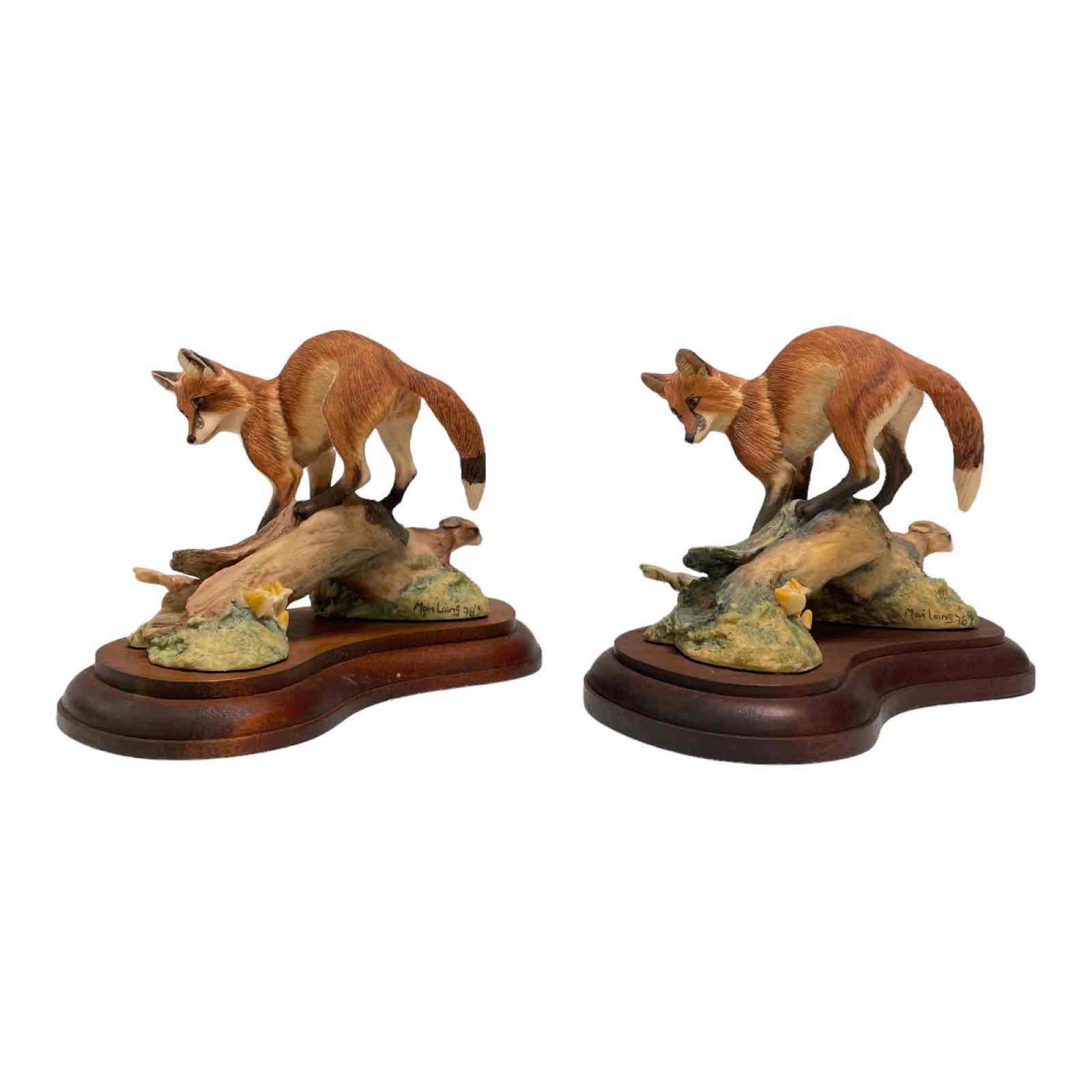 Two Artist Signed Laing Bordered Fine Art Red Fox: Two red fox perched on long with rabbit porcelain figurines by SCHMID Bordered Fine Arts and Artist Marie Laing 1978 signed and dated on verso as shown. Seated on walnut bases. Good condition, see pho
