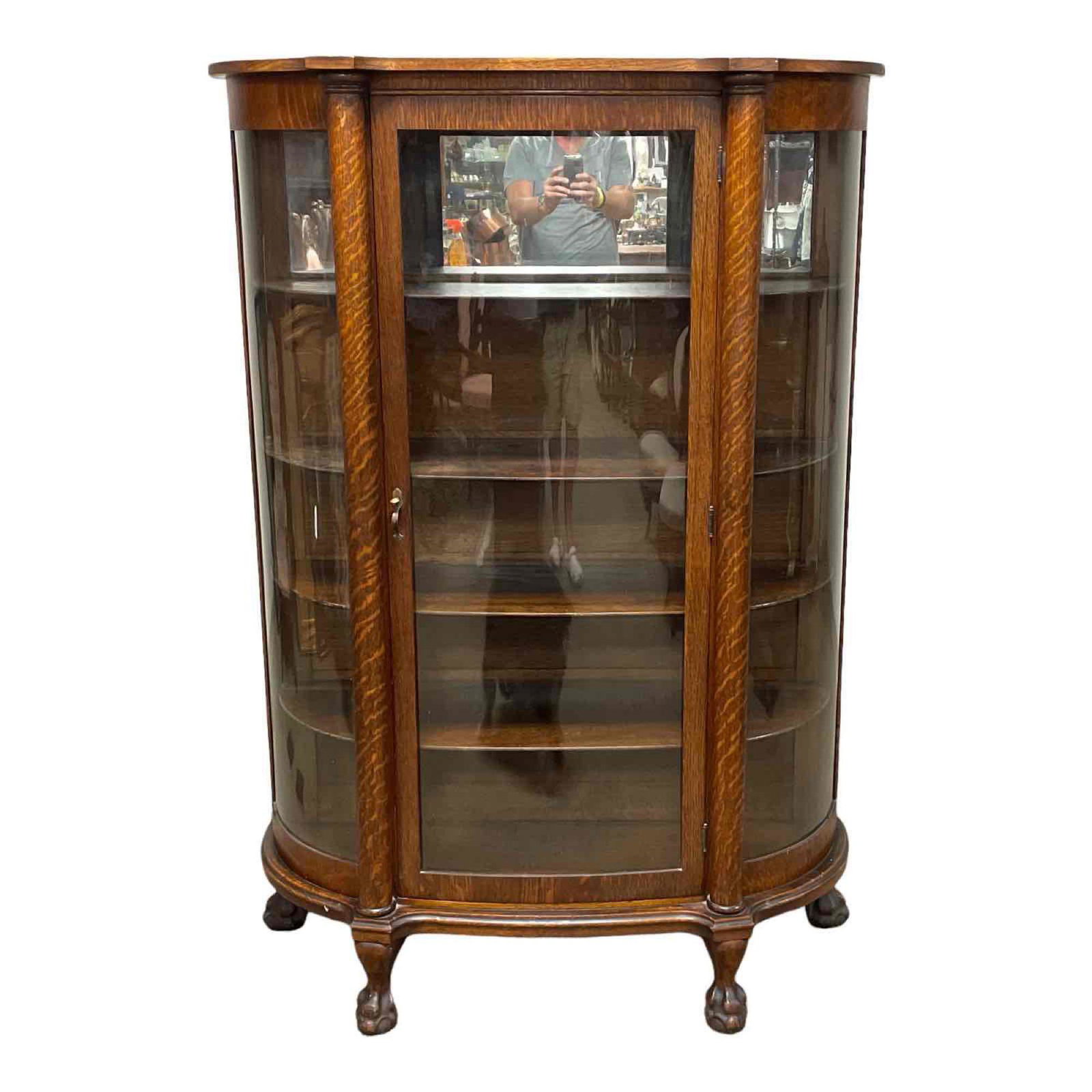 19th C. American Oak Ball and Clawfoot China Cabinet: Carved American Oak curved glass China cabinet with turned columns seated on ball and claw feet. Single center door and curved glass sides. Original oak finish, normal use and wear as shown, see photo