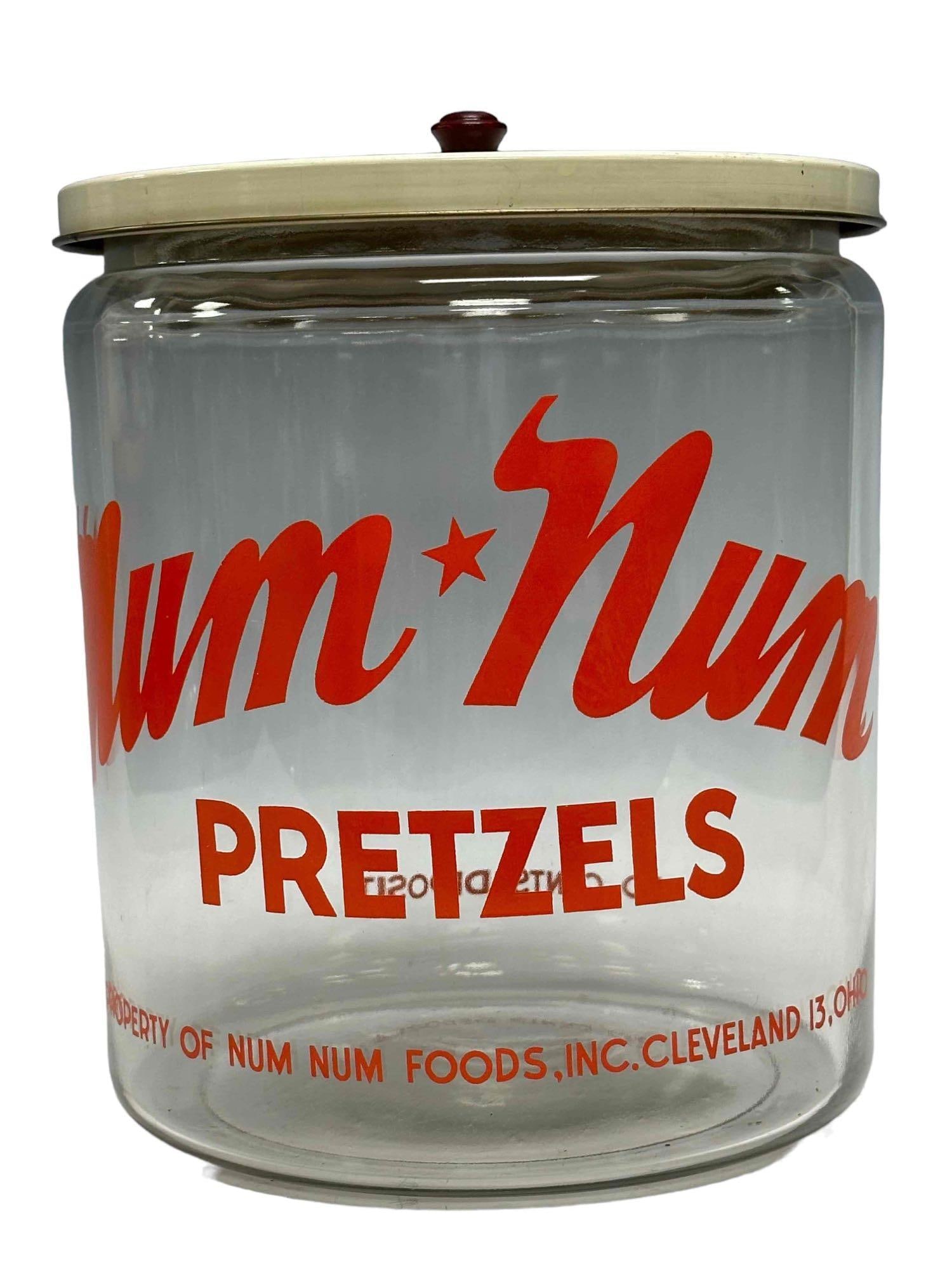 Vintage Num Num Pretzels Advertising Glass Jar: Vintage glass advertising country store jar with lid. Made in Cleveland Ohio. Normal use and wear, overall very good, see photos. Measuring approx 10 1/2" high and 8 1/2" diameter.