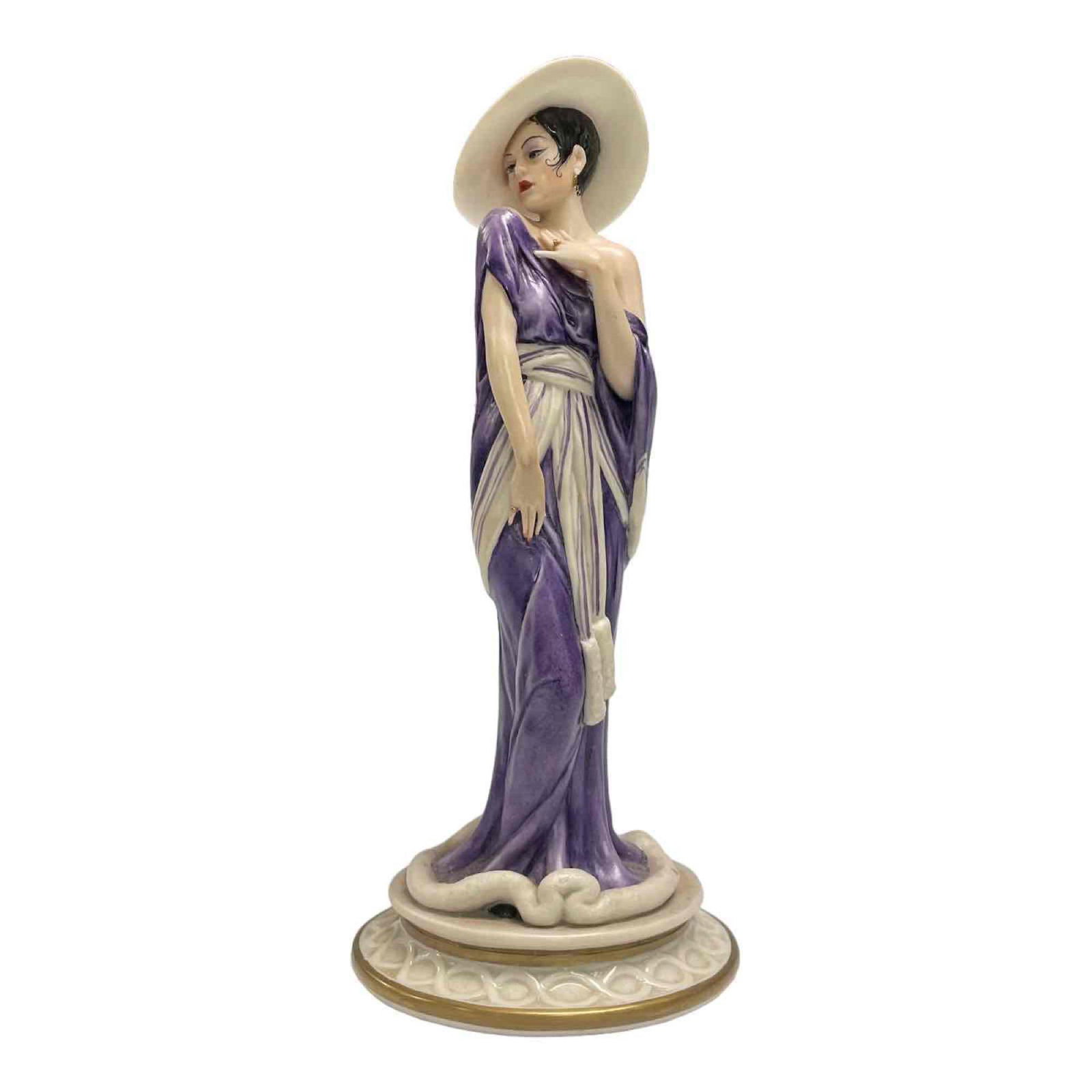 Sandro Maggioni Limited Edition Porcelain ANNO Figurine 126/5000: Porcelain Capodimonte Elite 1983, Mode Liberty anno 1930. Figurine of a lady in a purple dress and hat. Designed by Ceramist Sandro Maggioni. Standing approx 10" tall. Limited edition figurine 126/500