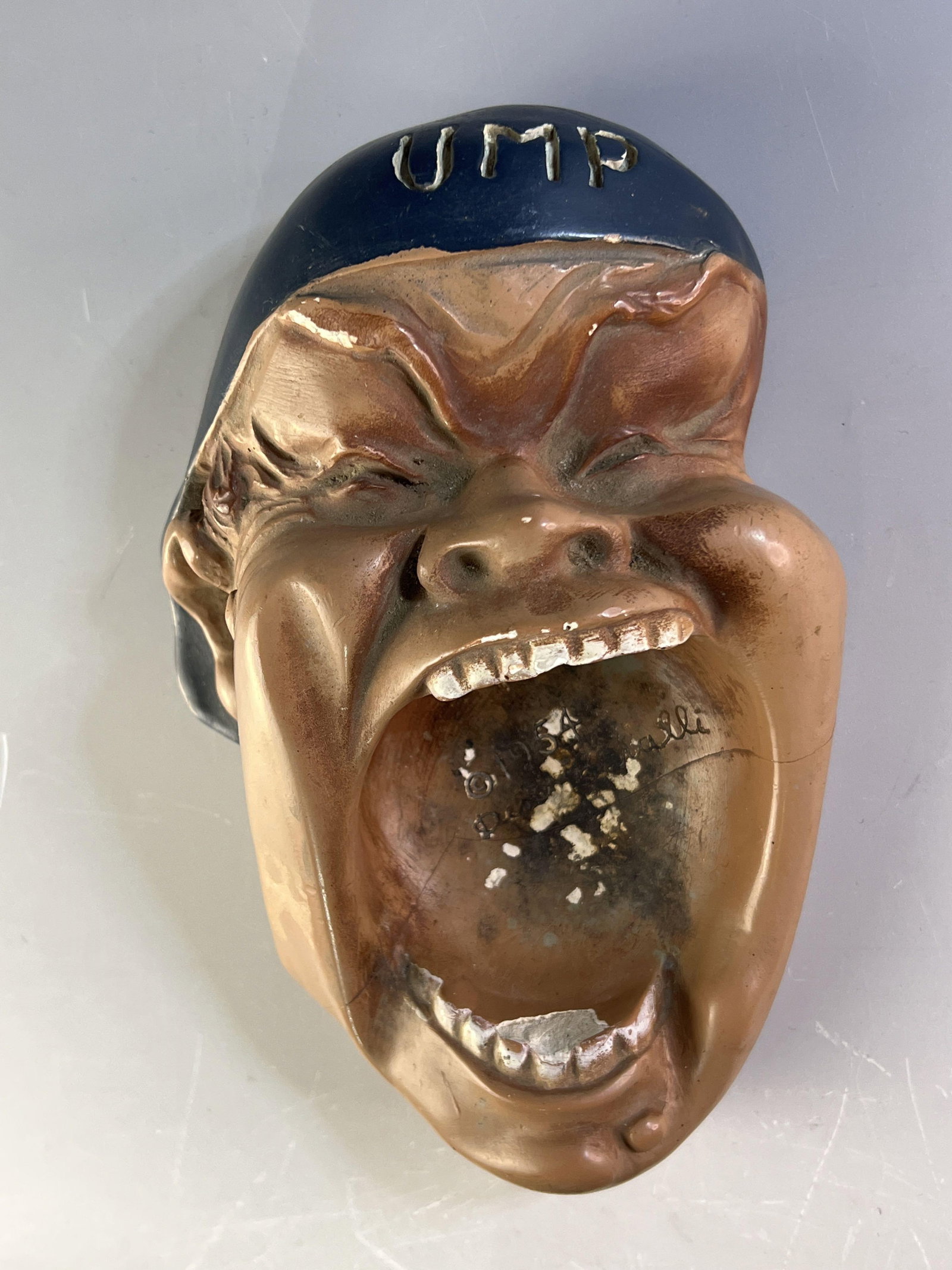 1954 Umpire Chalkware Ashtray Baseball: Chalk ware figure that is an "UMP" head yelling. Artist name is difficult to make out, but dated 1954. Heavy signs of use and light damage. Unique piece!