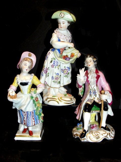 German/Meissen Polychrome Figures Late 19th. C.: In period dress. Saxony, of a gentleman and two ladies in various positions. Including lady in green hat gathering fruit in period dress with cross swords mark 5 1/2'' tall. Young lady in pink hat and