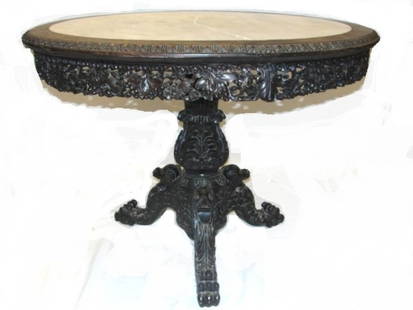 Carved Teak Wood Marble Top Center Table: Heavy carved round Oriental / Indo center hall or parlor table with inserted marble in a framed skirted top. Having a sectioned carved apron that’s wedged in by wooden pegs, that sits on a carved ba