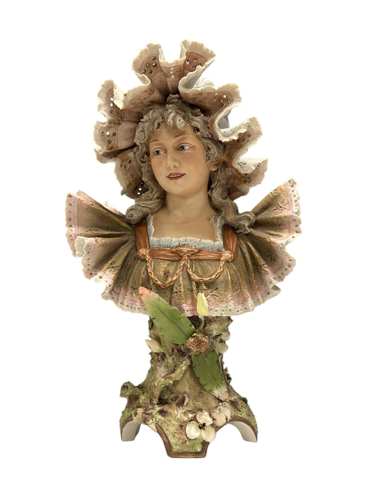 A Royal Dux Porcelain Bust of Maiden in Lace Bonnet: Elegant art nouveau Royal Dux Bohemia porcelain bust featuring a young woman. The waist- up bust stands 18.5" h x 12" w x 7" d. A very light rim nicks, overall very good as shown, see photos.