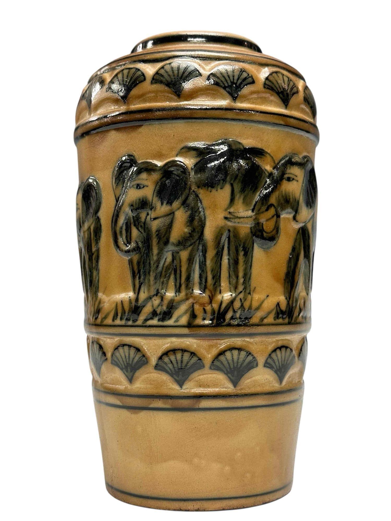 Elephant Motif Glazed Ceramic Vase: Raised relief glazed ceramic vase with elephant decor. Tan to light brown background with black elephant and fan motif. Measuring approx. 10" tall. In good condition with no breaks or chips noted, see