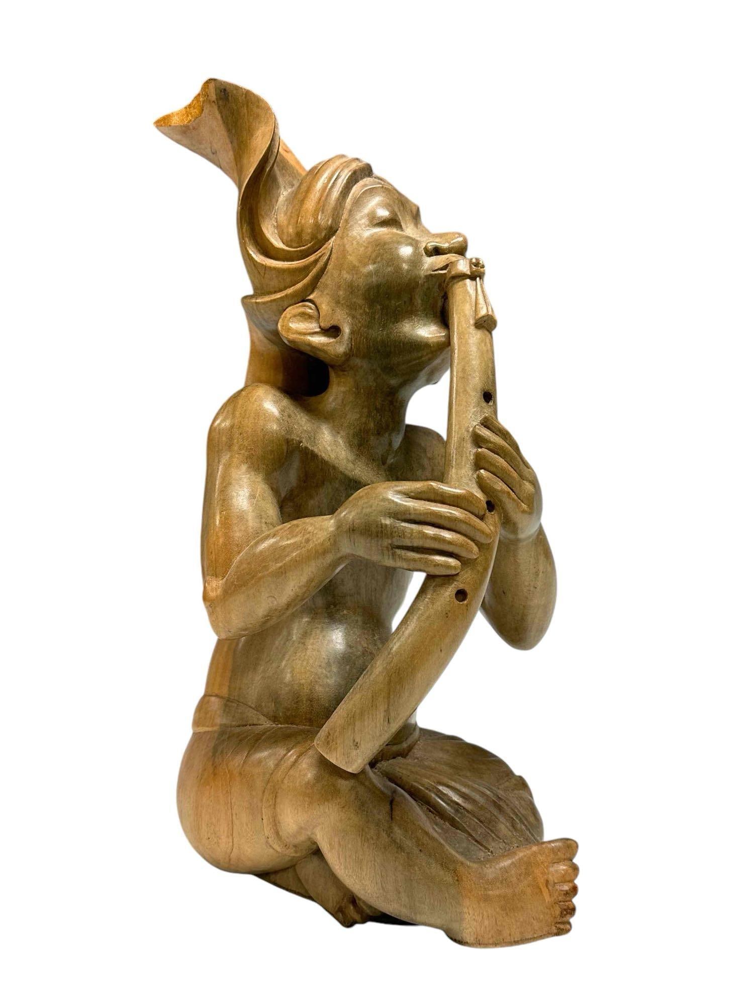 20th Century Balinese Wood Carved Flute Player Figural Sculpture: Beautiful and unusual wood carved sculpture of a stylized flute player. The sculpture sits upright on a flat surface. Age appropriate condition, head wrap has a large chip at end. Measures approx 15"