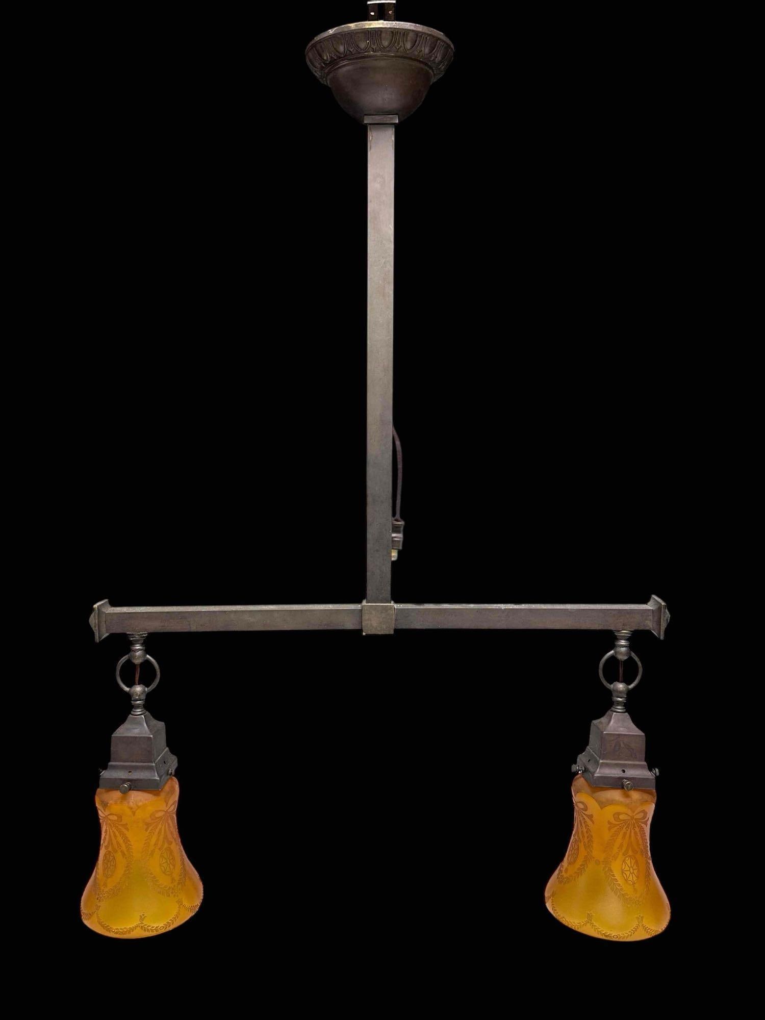 Arts and Crafts Style Two Light Amber Shades Chandelier Pendant Light Fixture: Inverted "T" form bronze finish two light chandelier/pendant electric light fixture. Square form structure with two bell form etched amber glass shades with ribbon and wreath decor. Measuring approx.
