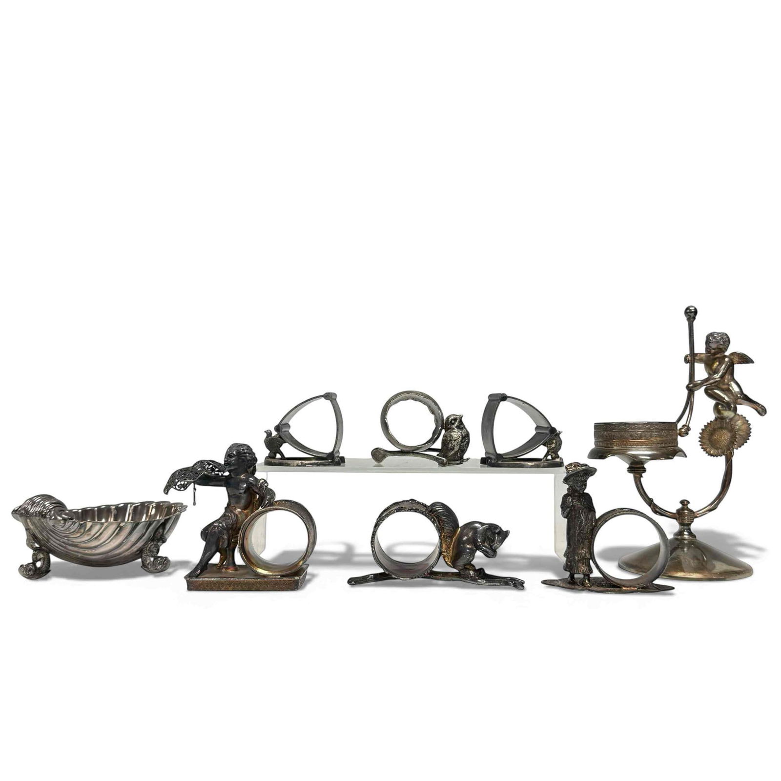Figural Silver Plate Cherubs Animals Shell Pieces (8): Includes six napkin holders with full figure squirrel, birds, horse shoe, cherub and young girl 2" to 3.75" tall, shell-shaped nut/candy bowl with dolphin/sea serpent style feet 2.5" tall by 5" long a