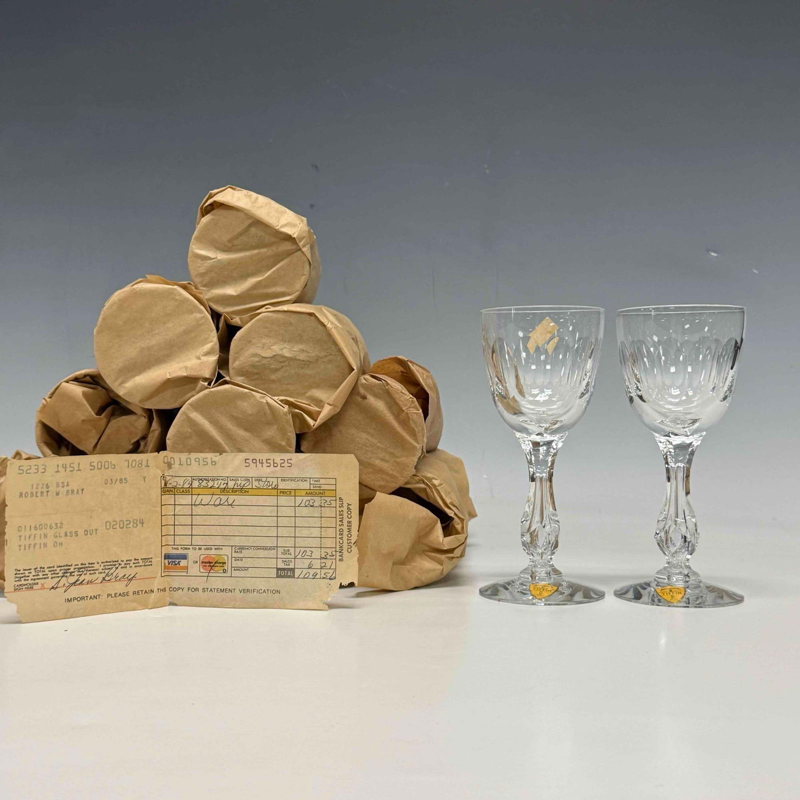 12 Tiffin Crystal Claret Wine Stems with Original Stickers: Set of twelve Tiffin-Franciscan cut crystal wine stems with vertical cut oval pattern and multi-sided cut stems. Having original yellow and gold Tiffin shield stickers tags. In good appear unused cond