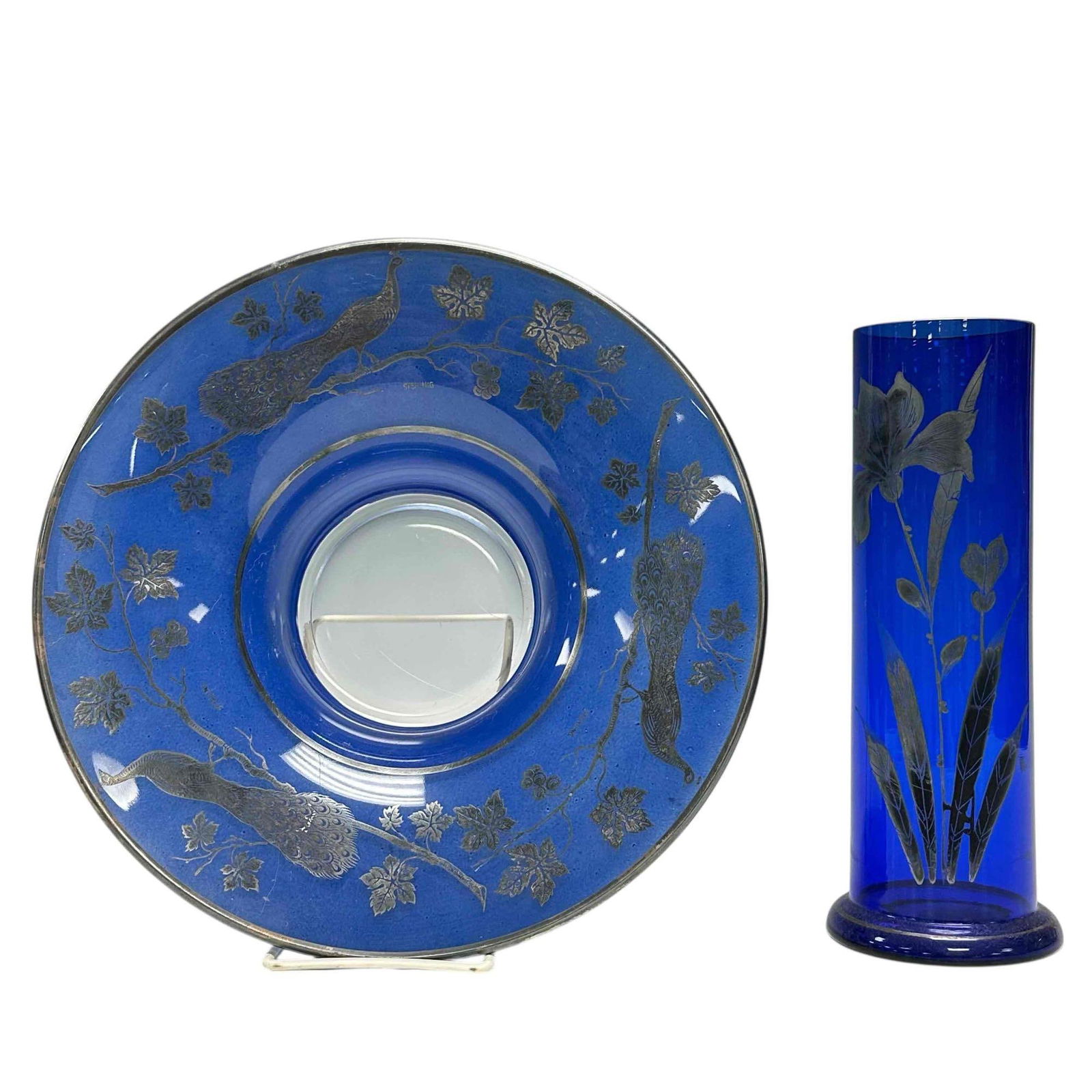 (2) Czech Cobalt Art Deco Glass with Sterling Overlay: Including a center bowl with peacock adorning the rim measuring approx 3" tall x 10" diameter and a cylindrical vase with flower motif approx 9.25" tall and stamped on bottom as shown. Light use and w