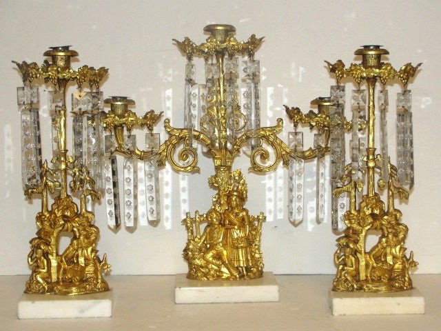 Victorian Figural Garniture Set With Prisms: Having center piece with 3 candle holder cups, young Ladd and girl on base and foliage and grape designs on top section on marble base. Missing 7 prisms. 16'' tall 18'' wide. Two single prism garnitur