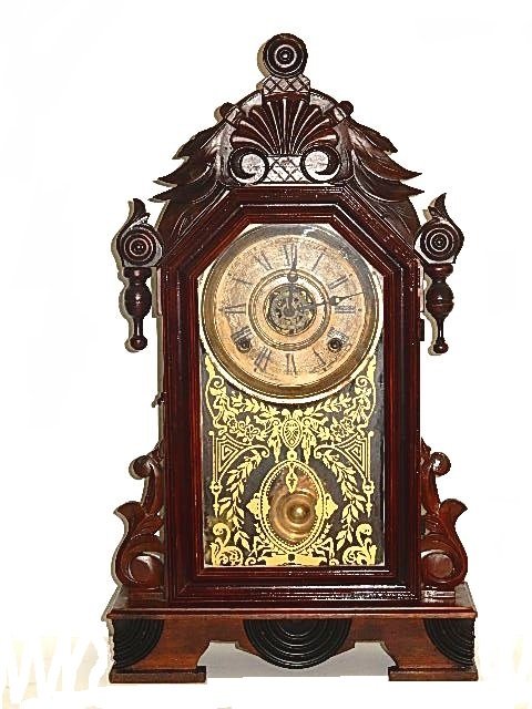 Carved Victorian Walnut Clock: Carved walnut case with gilded design front glass door, with alarm. Condition working may need cleaning, sometimes runs and stops. H. 22'' W. 12 1/4'' D. 4''. ''All Clocks Sold As Is''