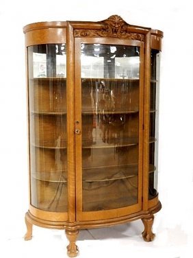 Oak Lion Head C.F. Curved Glass China Cabinet: Having crest of lion head, curved glass door and sides on claw feet. Condition good older refinish in honey oak color stain, piece of front foot missing and one back foot lightly loose with nail in su