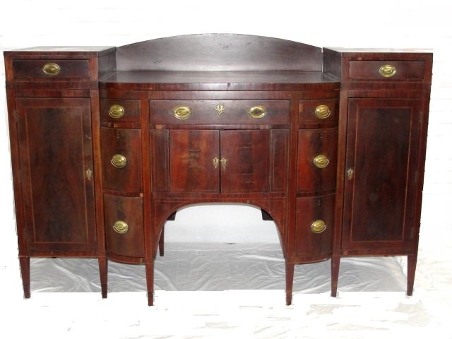 Early 19th. C. Mahogany Heppelwhite Sideboard: Having pedestal side cabinets with drop center with arched back splash string inlay throughout base. Two liquor cabinet drawers, silverware and candle drawers. Condition several veneer chips, one back