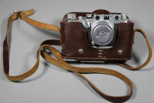 A Leica D.R.P Ernst Leitz Wetlar German Camera: Leica camera contained in its original Leica brown leather case with strap, No 496643. Wear to case and strap showing its signs of use. Camera functions, shutters and mechanics seem to move freely. So