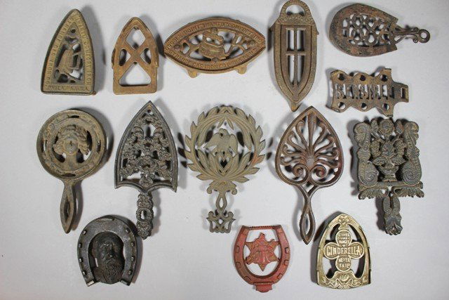 Group of 14 Cast Iron Trivets: Group from late 19th century through the early 20th century. Including several ornate handled trivets as well as traditional embossed designs as shown. Various NY, Chicago, Ohio and others. Normal use