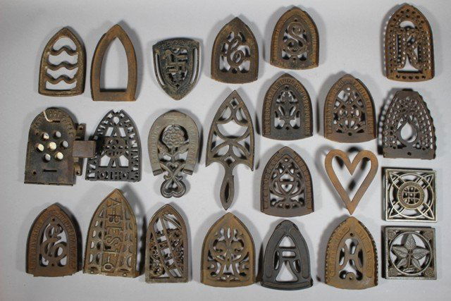 Group of 22 Sade Iron & Stove Cast Iron Trivets: Various sizes and shapes as shown. Some having more ornate details. Largest approx. 7" down to 3.5". Normal use and wear. Various state and makers marks.