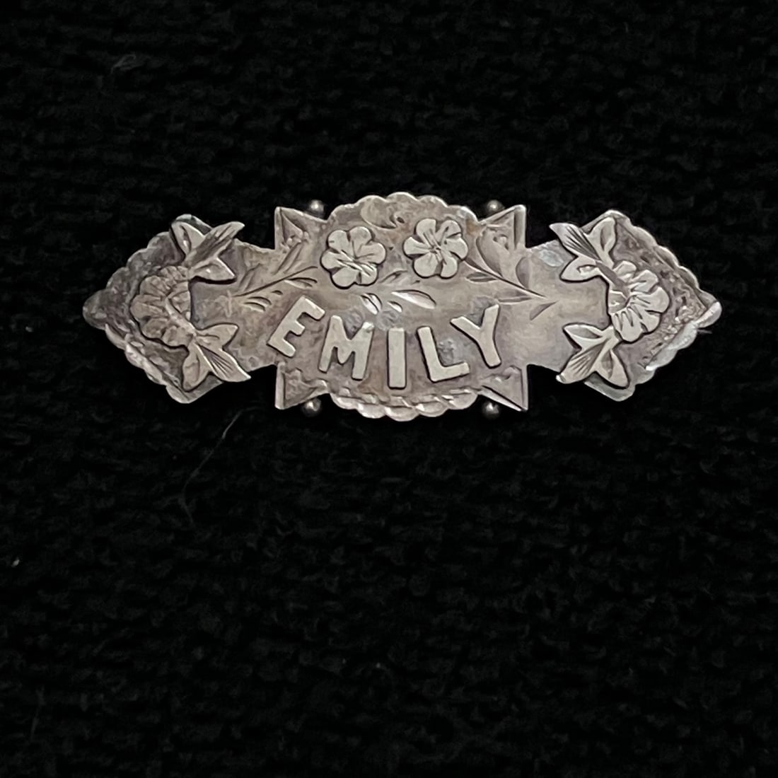 Sterling Silver Brooch w/ name Emily: Small personalized brooch with raised “EMILY” lettering and floral decoration in silver-tone metal. Reverse shows a tube hinge, straight pin, open C-clasp, and several partially legible
