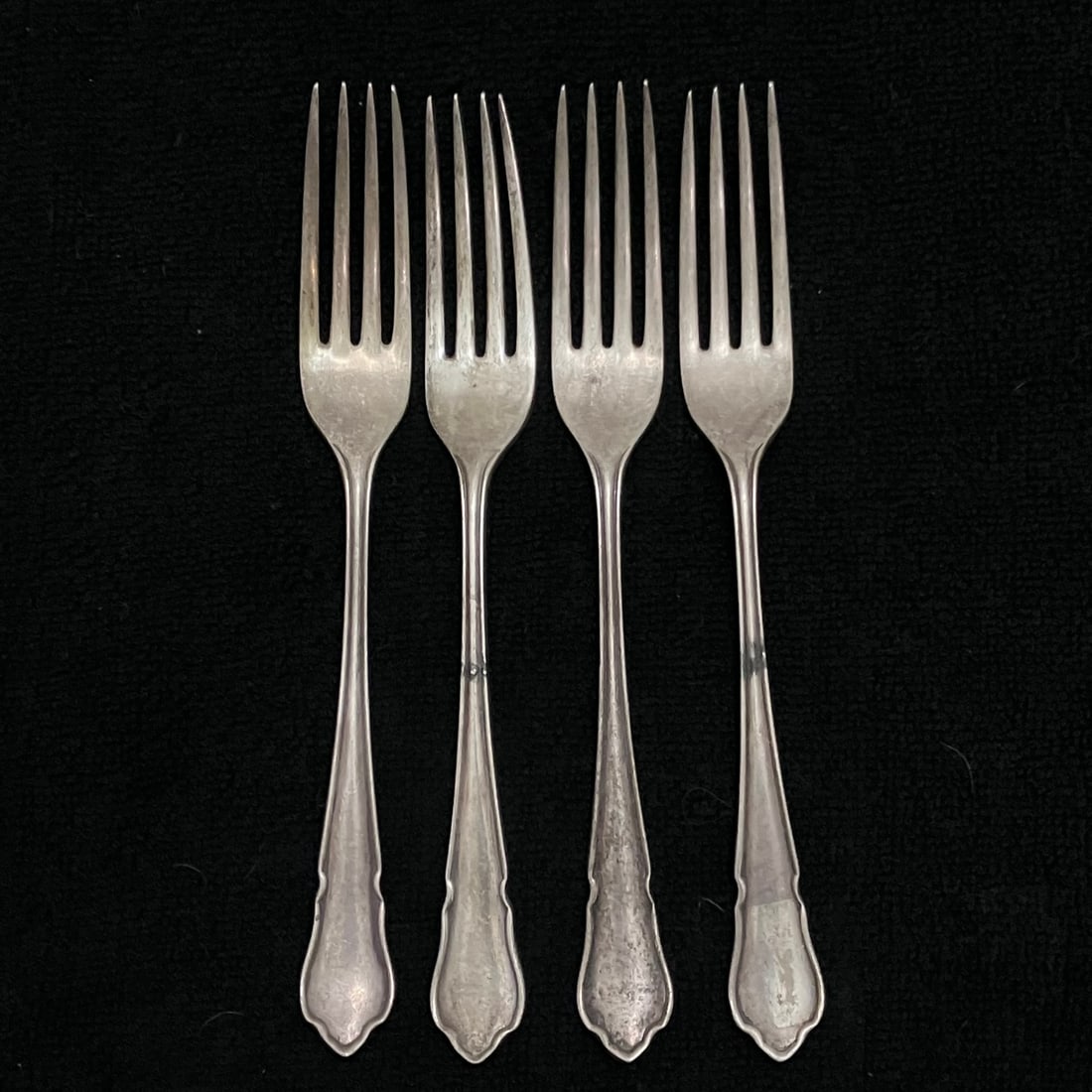 Hallmarked Sterling Silver Dessert Forks 220.4 g: Set of four matching hallmarked silver forks with plain tapered handles and four-tine heads. Reverse handles show a maker’s mark reading B&H or B & H, along with additional British-style hallmarks