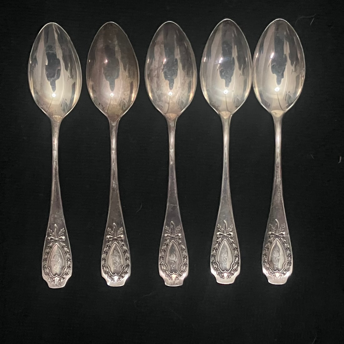 Sterling Silver Teaspoons Set - 105.4 g: Set of five matching small spoons with oval bowls and decorated handles featuring a wreath-and-bow motif and monogrammed front cartouches. Backstamps include a partially legible “STERLING” mar