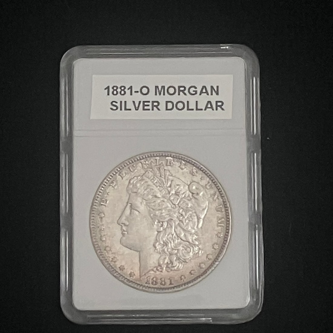 1881-O Morgan Silver Dollar: U.S. Morgan dollar coin showing the date 1881 on the obverse and an apparent O mint mark on the reverse. The coin is housed in a generic clear plastic holder with an insert labeled “1881-O MORGAN
